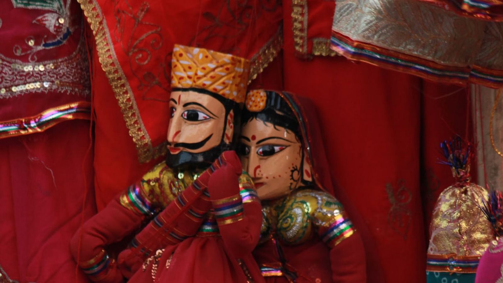 Rajasthani puppets, dressed in traditional attire with intricate details, are displayed against a backdrop of vibrant fabrics.