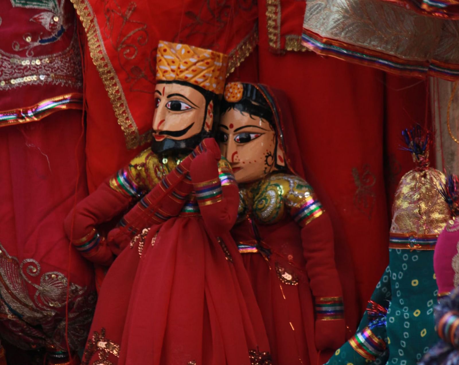 Rajasthani puppets, dressed in traditional attire with intricate details, are displayed against a backdrop of vibrant fabrics.