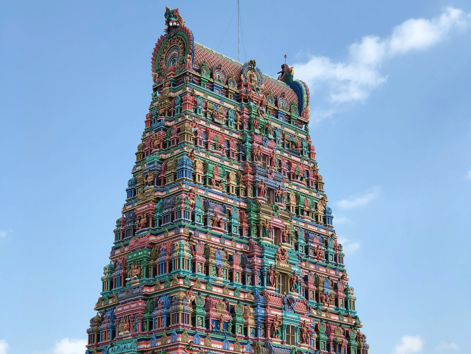 A towering, colourful temple gopuram rises against a clear blue sky - Grand Madurai by GRT hotels.