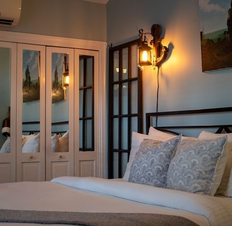 A bedroom with metal headboard, blue patterned pillows, maritime artwork and lantern sconces at Hartstone Inn.