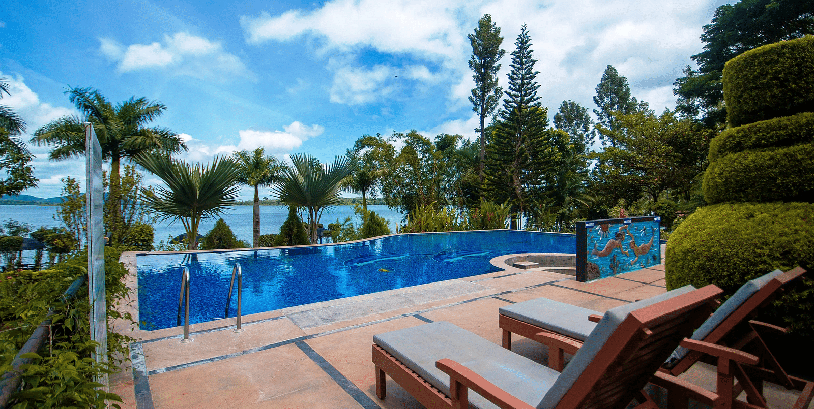 Sun loungers placed facing the outdoor swimming pool and the seascape bordered by greenery at  Coorg Jungle Camp Backwater Resort in Kushalnagar