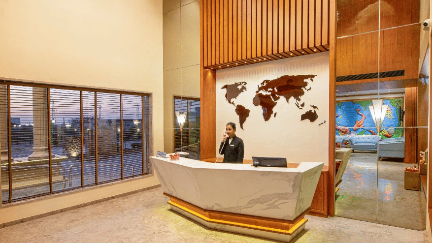 A modern hotel reception with wooden panelled wall on one side and a chandelier hanging overhead at Lords Inn Jamnagar