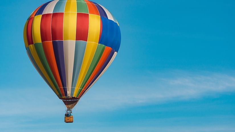 a solitary hot air balloon soaring in the sky with white clouds in the blue sky visible