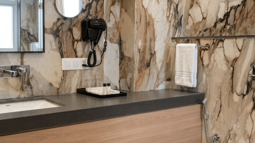A modern bathroom features marble walls, a wooden vanity, and a clean toilet - Pride Elite Himmatnagar, Gujarat