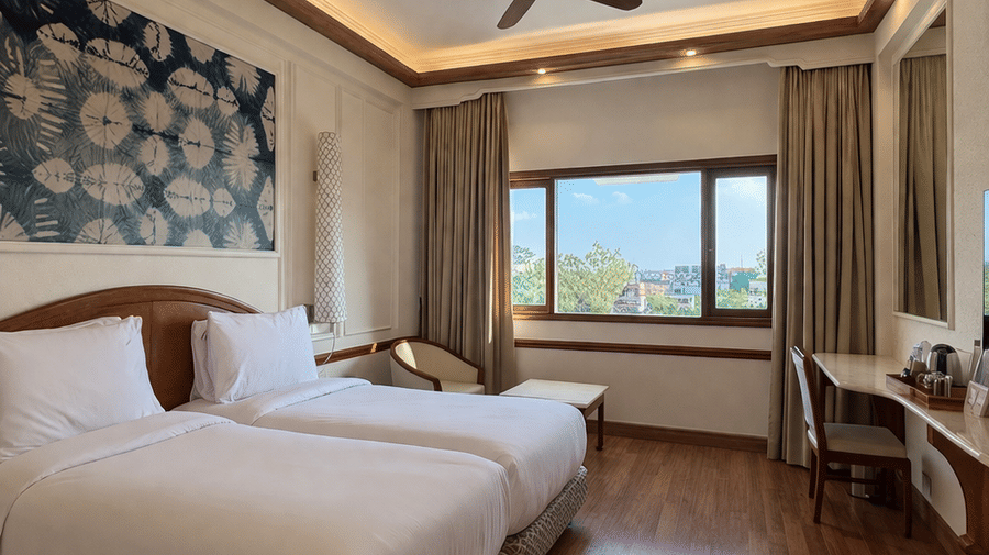 Twin beds with patterned bases are arranged under a ceiling fan and recessed lighting in the Deluxe Twin room at Clarks Amer, Jaipur.