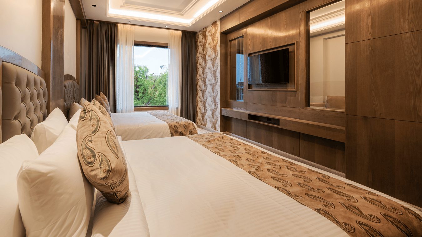 A spacious guest room with two single beds, dark wood wall panelling, and a large window at Ananta Express, Katra.