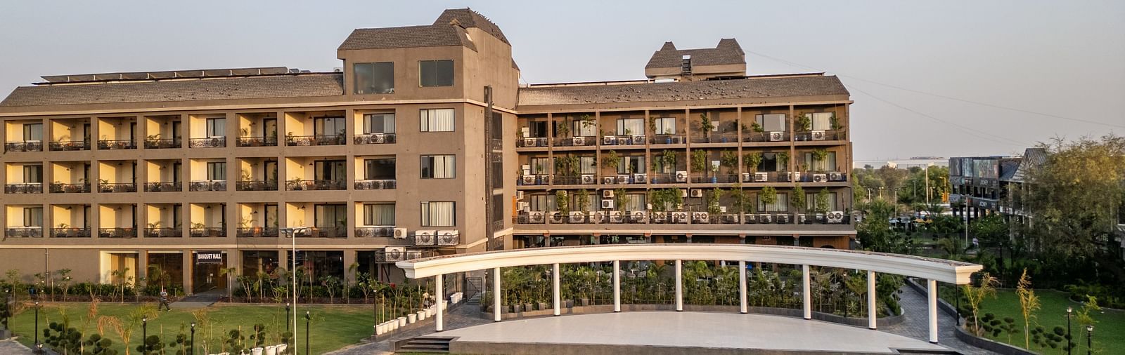 Hotel Highway King, Bagru, building with multiple balconies and a large green lawn in front under a clear sky. 