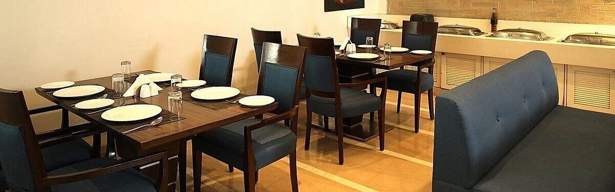 Tables and chairs neatly arranged with cutlery set on the table at Café Inde, Inde Signature Tower, Gurgaon