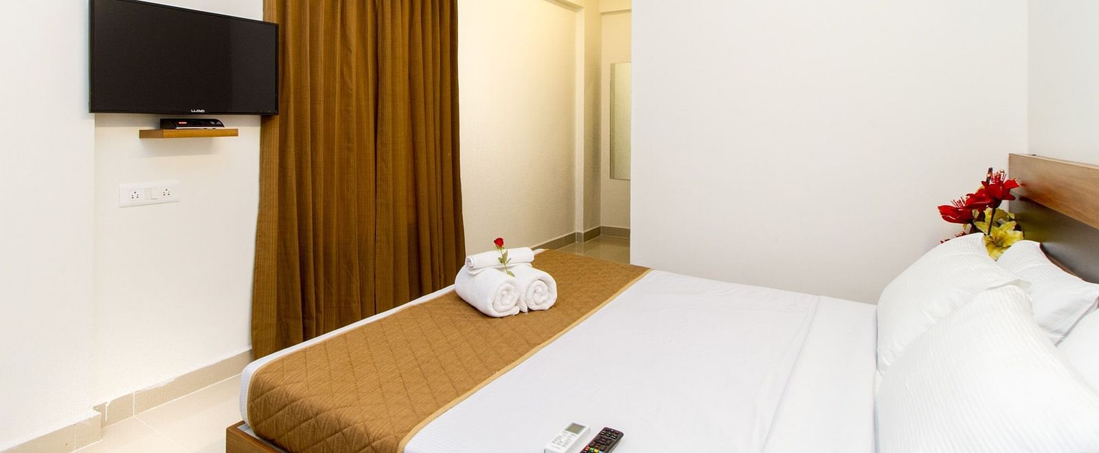 A hotel room at Sanctum Suites Whitefield, Bangalore featuring a bed with brown and white bedding and a wall-mounted television.