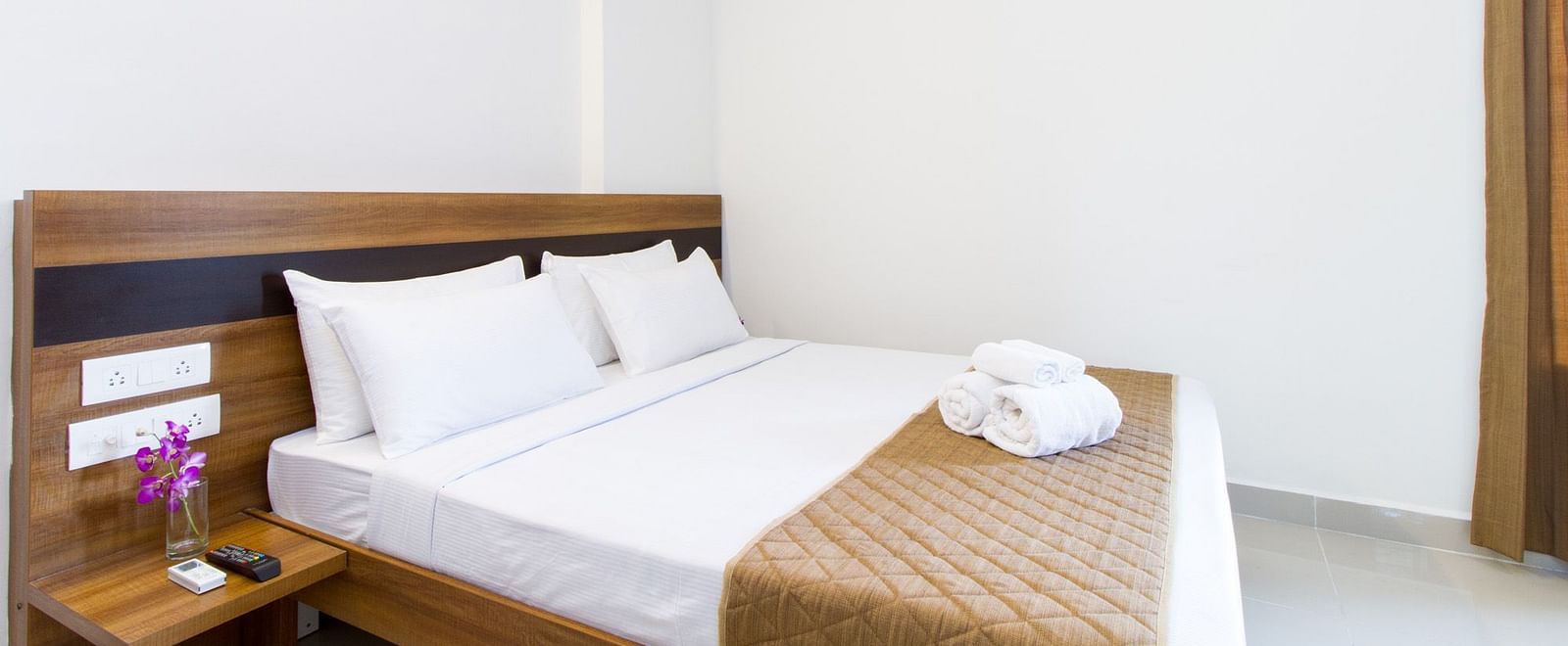 A tidy hotel room at Sanctum Suites Whitefield, Bangalore providing a double bed with neatly folded towels and bedside tables.