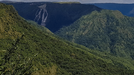 A beautiful landscape of Shillong featuring lush green mountains with a bright blue sky and distinctive clouds floating over it.