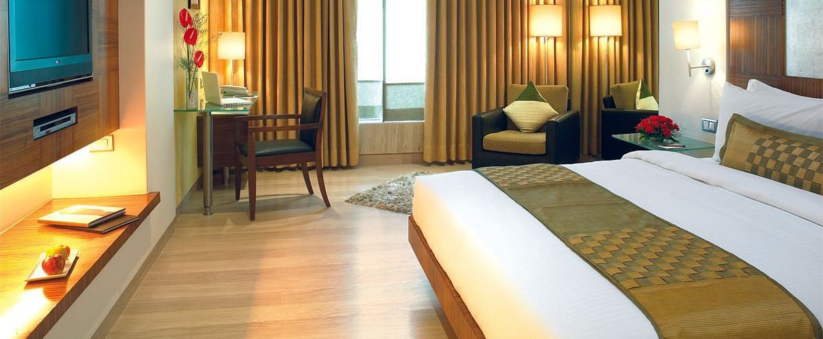 Image of a the executive room featuring a king size bed, a study table and chair, flat screen television, and an expansive window with golden curtains. | Mirage Hotel