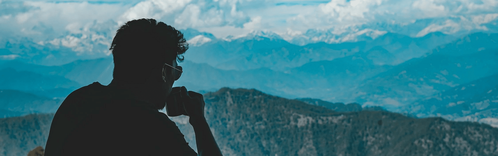 A man sipping a drink looking at the mountain view in front