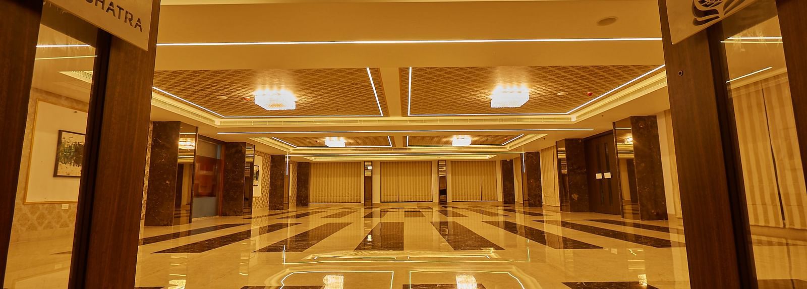 A long perspective of an empty, well-lit banquet hall with glossy, patterned floor tiles and decorative ceiling details.