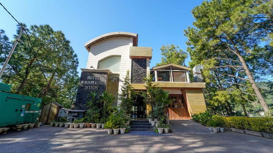 A facade image of DLS Whispering Winds surrounded by trees with a clear blue sky in the background