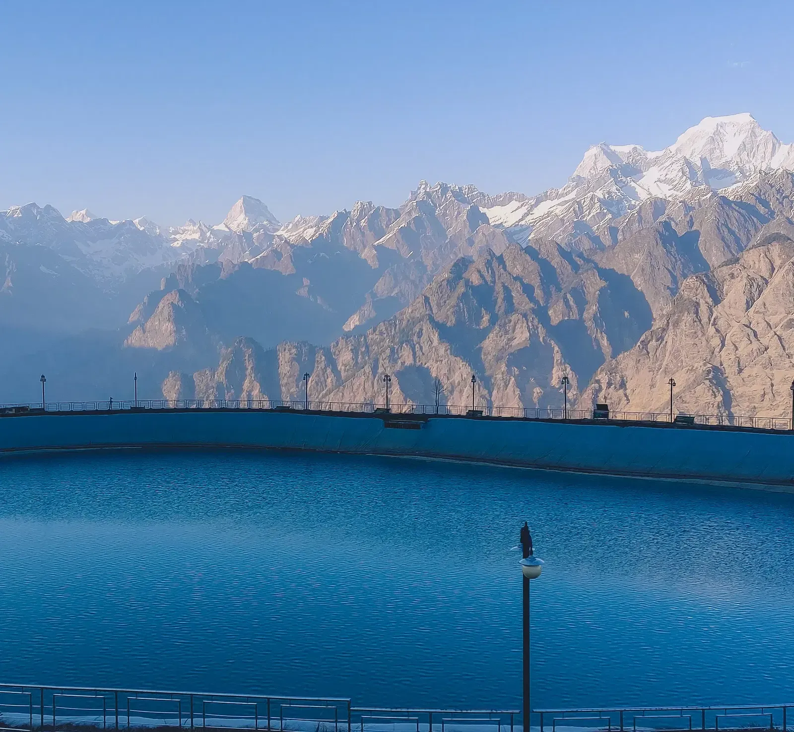 A serene blue lake reflects a rugged mountain range under a clear sky.