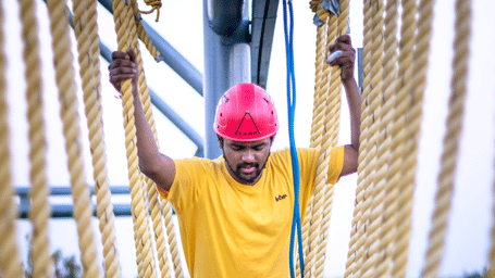 A smiling man in a red helmet navigates a challenging thick rope course - District Gravity Adventure Park, Hyderabad