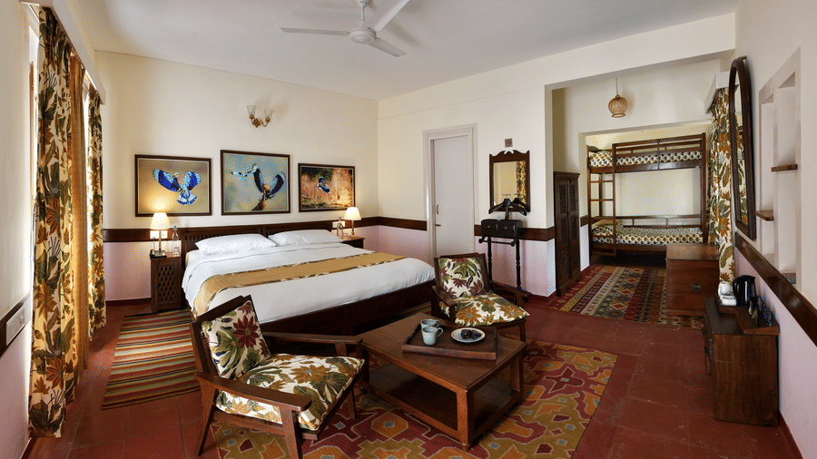 Large suite bedroom featuring a central bed wooden wardrobes side seating area traditional flooring and multiple windows offering ample space and relaxation at Neemrana’s Glasshouse on The Ganges ideal for guests seeking comfort and openness