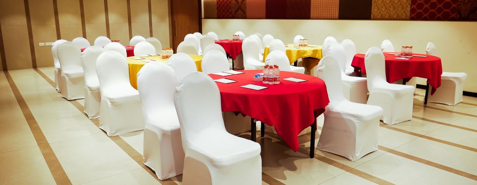 A well decorated banquet hall set up with round tables draped in red, ready for an event at Shilton Dee Cee.