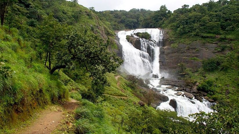 Large waterfall in a green forest with a footpath on the left