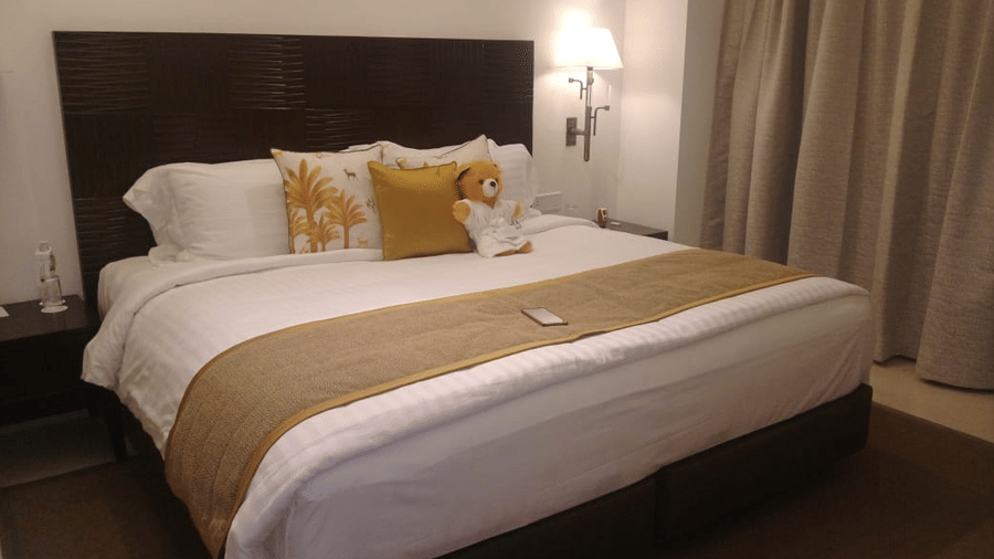 The Mansion House cozy hotel bedroom with neatly made bed, white sheets, decorative pillows, beige runner, remote control, and warm lighting, showcasing elegant hospitality and interior decor.