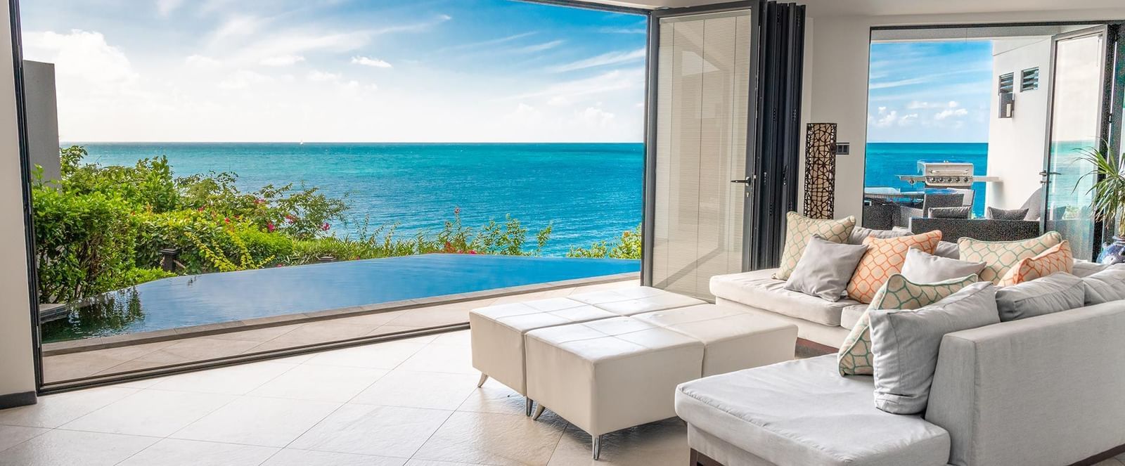 The modern villa at Tamarind Hills Antigua with sofas and colourful pillows, open doors showing a private pool and the blue Caribbean Sea - Tamarind Hills Resort and Villas - Antigua