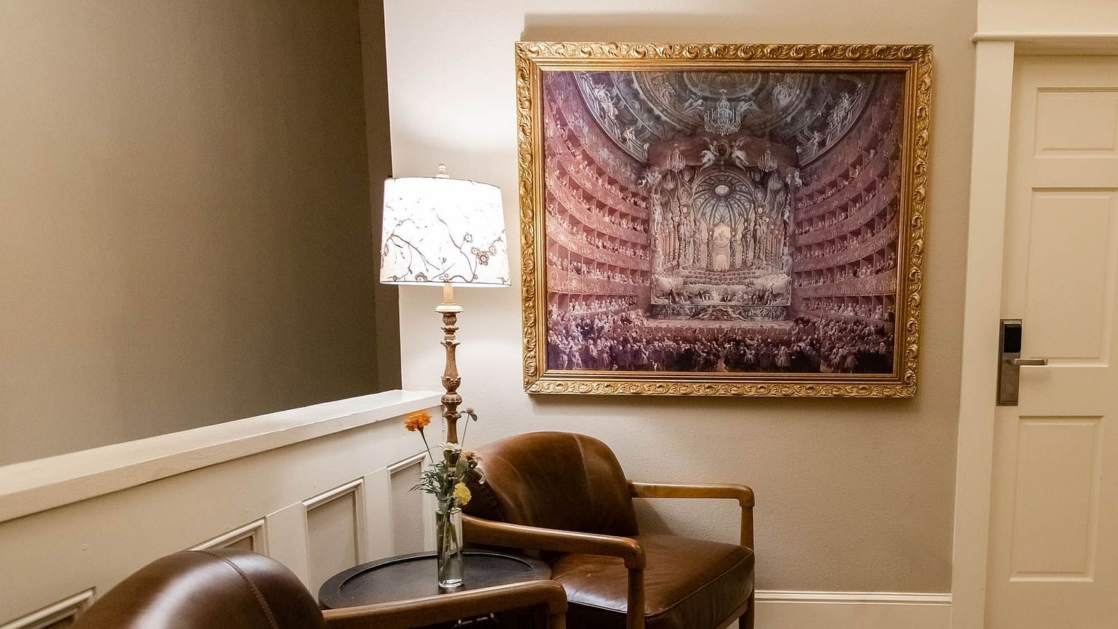 A cozy seating area features two armchairs, a side table with a lamp, and a framed patterned artwork on the wall.- The Grand Hotel & Ballroom, McKinney