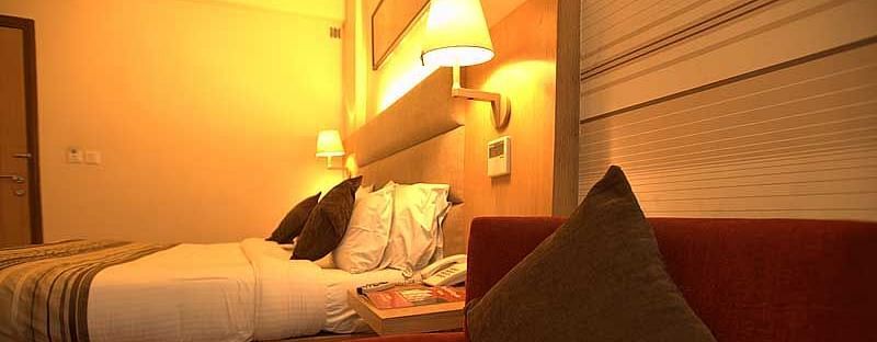 An image of a superior bedroom at The Manor, Bareilly, illuminated by warm yellow light from a stylish lamp
