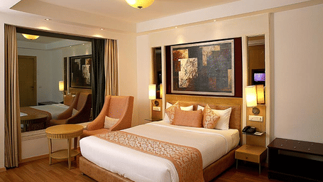 A spacious double room at Eastlynn Collections HUDA City Centre, Gurugram featuring a large bed, seating area, warm lighting, and modern decor.