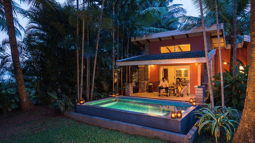 Evening view of The Residence at The Serai Kabini showing a covered patio, seating area, and a private swimming pool surrounded by trees.