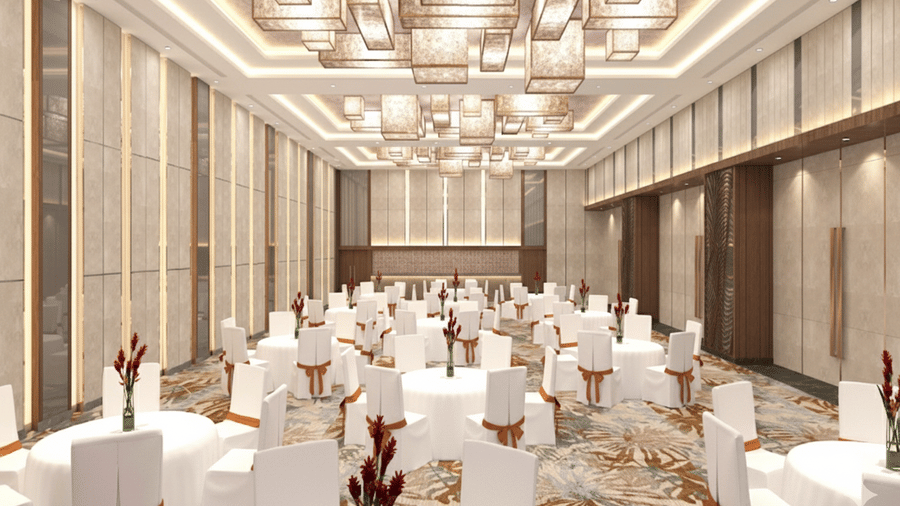 Render of interior of a large banquet hall at Vandhara Sarovar Premiere, Patkote, with clothed round tables, chairs, and modern rectangular chandeliers.