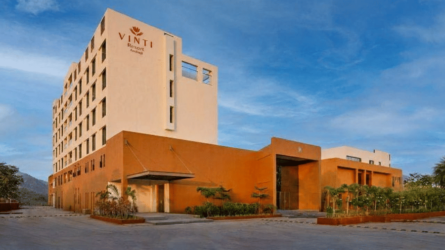 The striking exterior of Vinti Resort, Ambaji, showing the cream-coloured tower and terracotta-hued base under a blue sky.