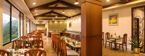 Restaurant interior showing a long row of tables and chairs. The room has large windows, wooden pillars, and exposed wooden beams - Abad Copper Castle, Munnar