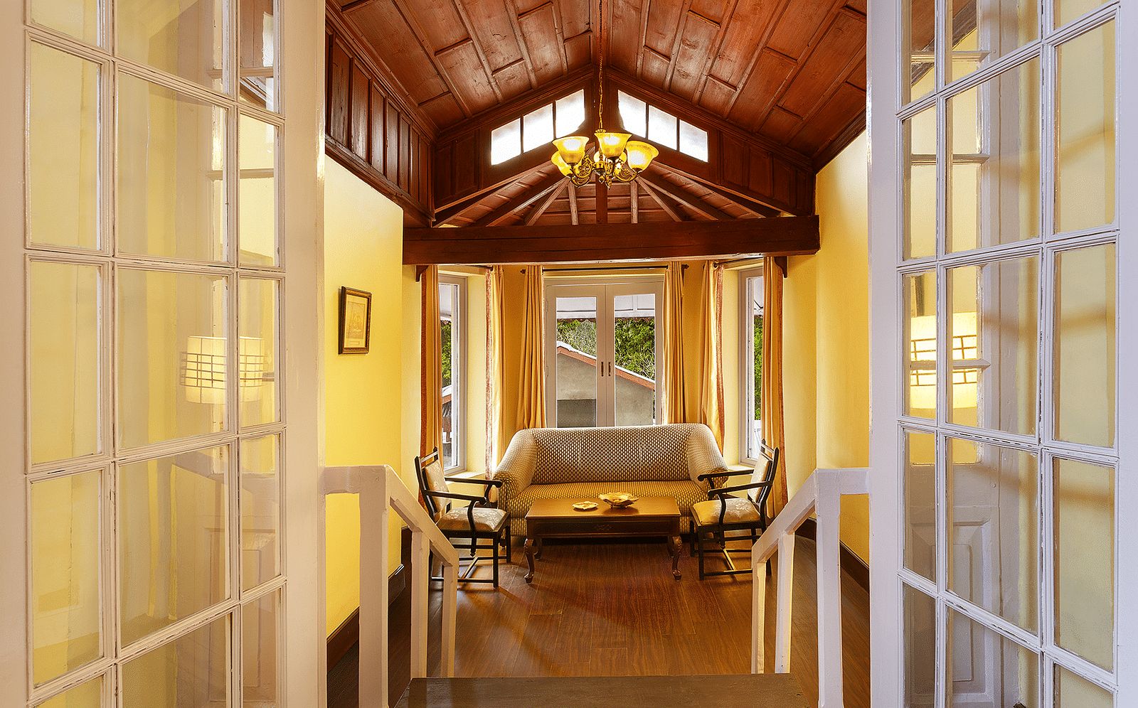 a hallway with a sofa on the far end and a chandelier hanging from the ceiling - The Earl's Court, Nainital