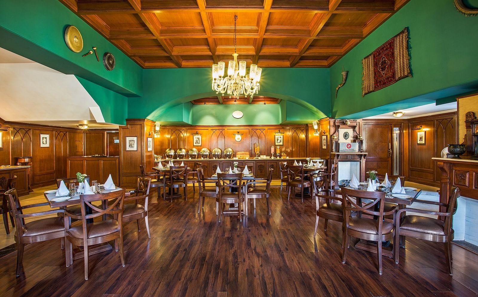 An image showing the interior of restaurant at The naini retreat, Nainital. featuring wooden decor, flooring, and a wooden bar. A large chandelier hangs from the ceiling, providing ambient lighting.