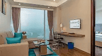 A bright area with a couch and cushions on it under a colorful carpet and a unique chair beside it. - Golden Suites, Gurgaon