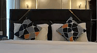 A bed with a textured headboard and decorative pillows. Lighting creates a warm ambiance.- Golden Suites, Gurgaon