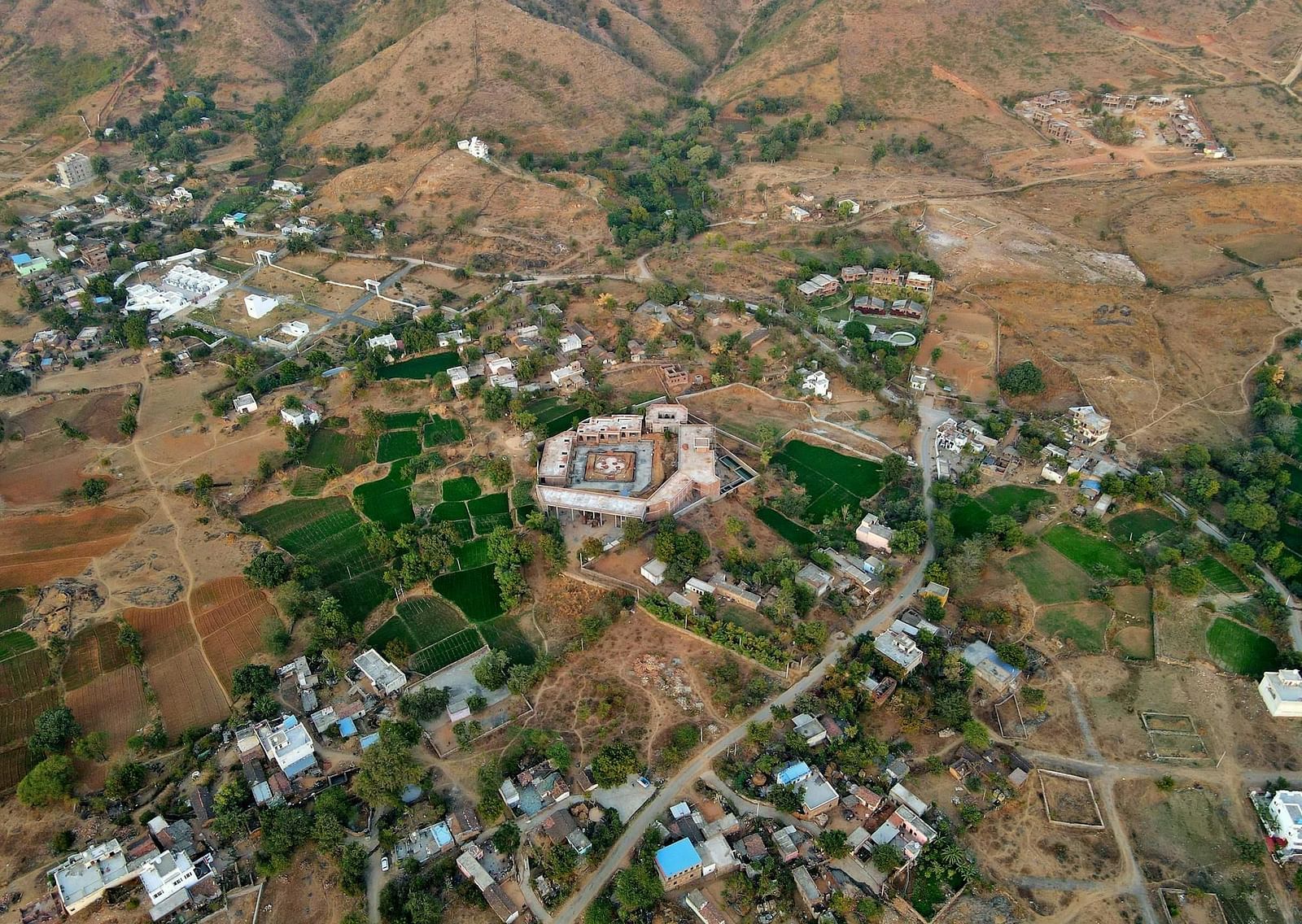 An aerial view of a the monsoon palace in Udaipur surrounded by a rural landscape with fields and hills.