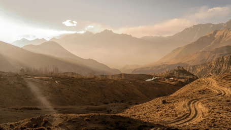 A sweeping, sun-drenched view of the rugged mountain valley landscape and winding dirt roads in Mustang region, Nepal.
