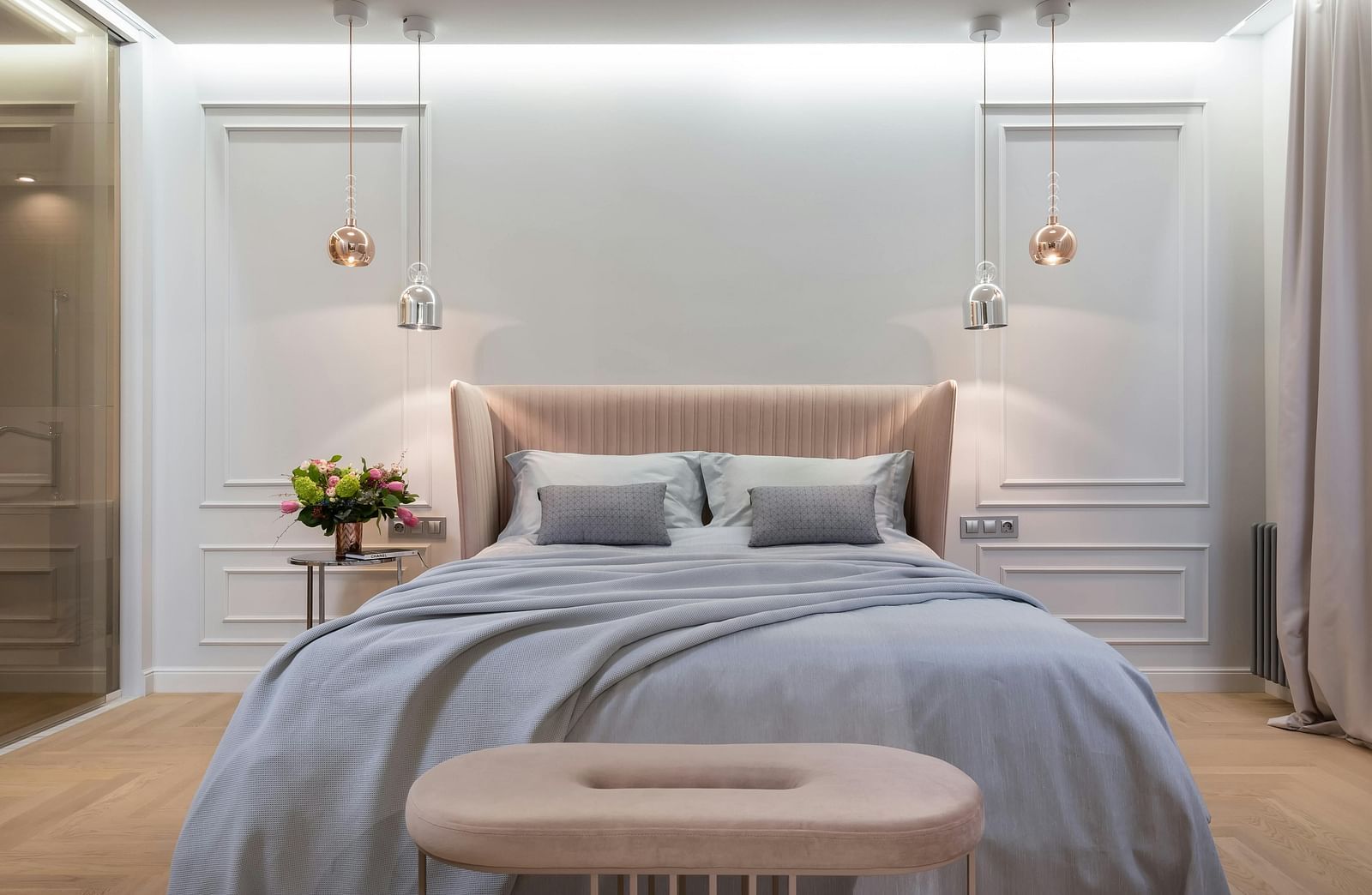 A modern bedroom is shown with soft lighting, a grey duvet, and a tufted bench.
