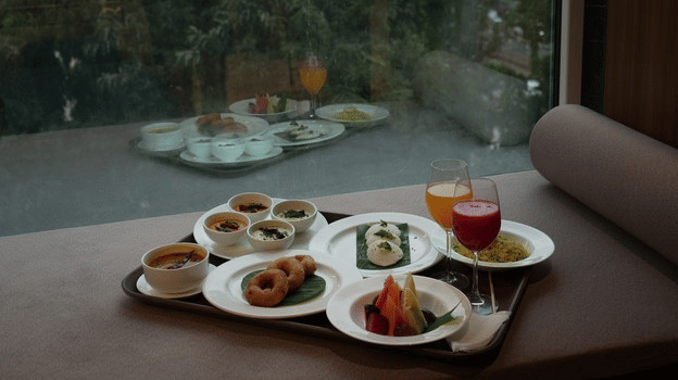 Assorted dishes and beverages served at a window-side dining table with garden views at Pride Premier, Pune.