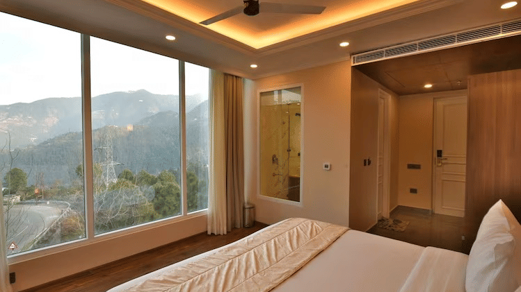 Cosy room with a double bed, wooden flooring, and panoramic hill views through large windows at Claret Inn, Dalhousie.