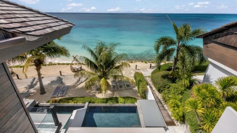 A luxurious villa with a private pool and outdoor seating areas overlooking the ocean and palm trees.