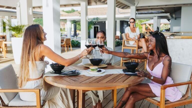 Three women are seated at a wooden table outdoors, enjoying drinks and conversation.