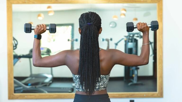 A woman exercising with dumbbells looking at a mirror in a well-equipped gym.