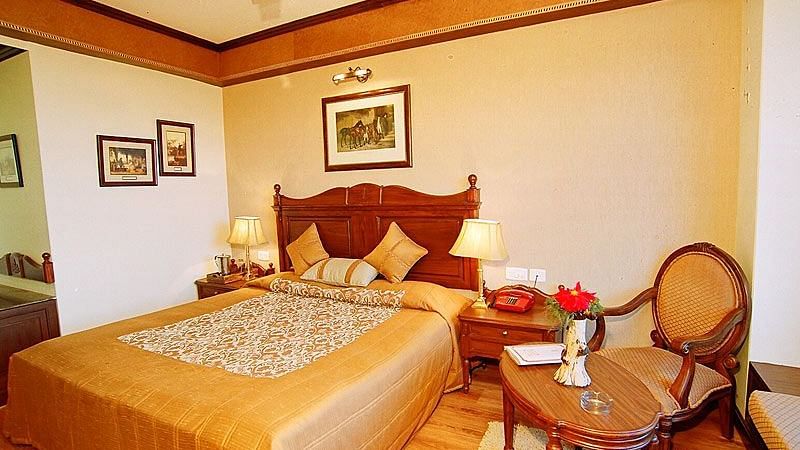 View of a bedroom with a small table and chair and a bed with side drawers on each side - Sun N Snow Inn, Kausani