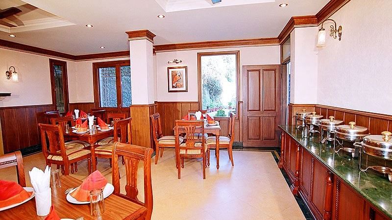 A restaurant with a buffet setting on the right side and tables with chairs arranged in clusters  across the room - Sun N Snow Inn, Kausani
