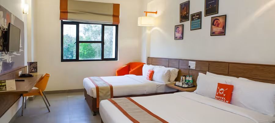 View of a hotel room featuring two comfortable beds, wall art, and a large window with natural light - Max Hotel Prayagraj.