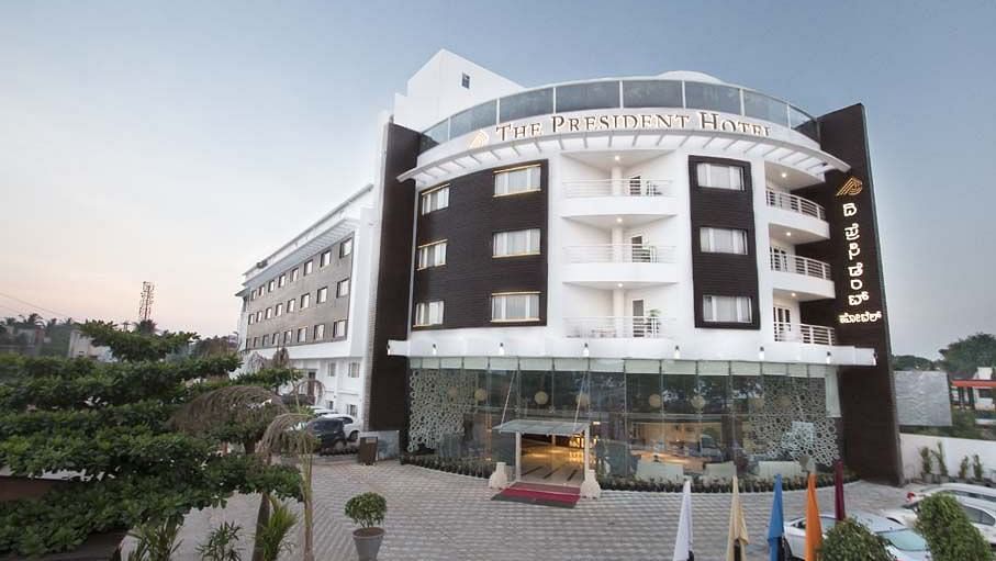 A facade image  with a huge parking area where cars are also parked - The President Hotel,Hubli