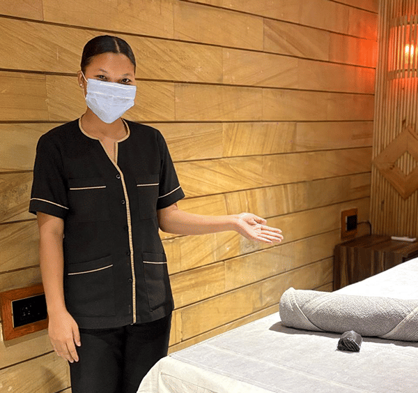 SKYN Spa therapist in a black uniform welcoming guests beside a treatment bed